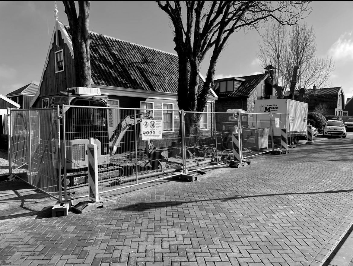 Minigraver achter bouwhekken bij een groen houten huis
